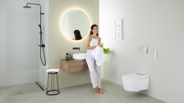 Žena opierajúca sa o umývadlo v kúpeľni so sprchovacím WC Geberit AquaClean Sela a umývadlom a kúpeľňovým nábytkom Geberit VariForm