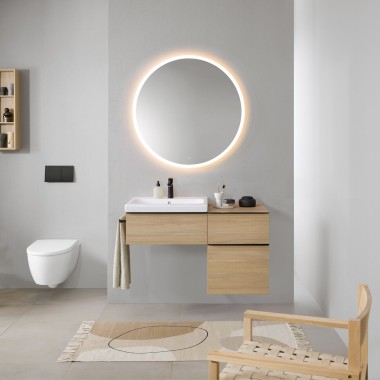 Kúpeľňa so sivými stenami, kúpeľňovým nábytkom Geberit z dreva a okrúhlym osvetleným zrkadlom Geberit Option