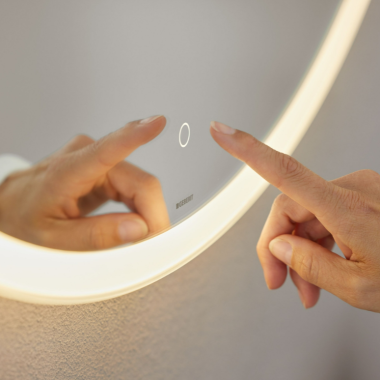 Ruka ovláda spínač s dotykovým senzorom priamo na zrkadle Geberit Option Round (© Geberit)