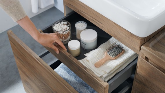 Ruka otvára jednu zo zásuviek umývadlovej skrinky v dizajne prírodného dreva