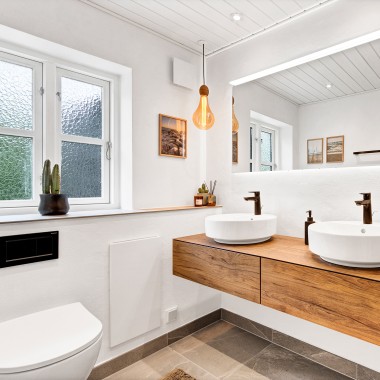 Svetlá zrekonštruovaná kúpeľňa s dvoma okrúhlymi umývadlami, veľkým zrkadlom a dreveným kúpeľňovým nábytkom (© @triner2 a @strandparken3)