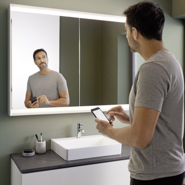 Muž ovláda osvetlenie zrkadlovej skrinky Geberit ONE pomocou smartfónu (© Geberit)